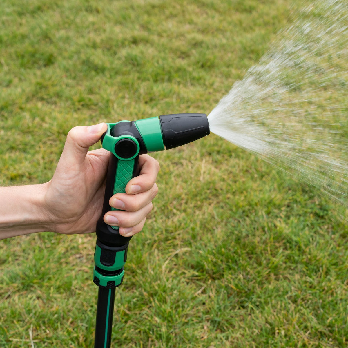 Hand hält die Gartenpistole und bewässert den Rasen mit breitem Sprühstrahl