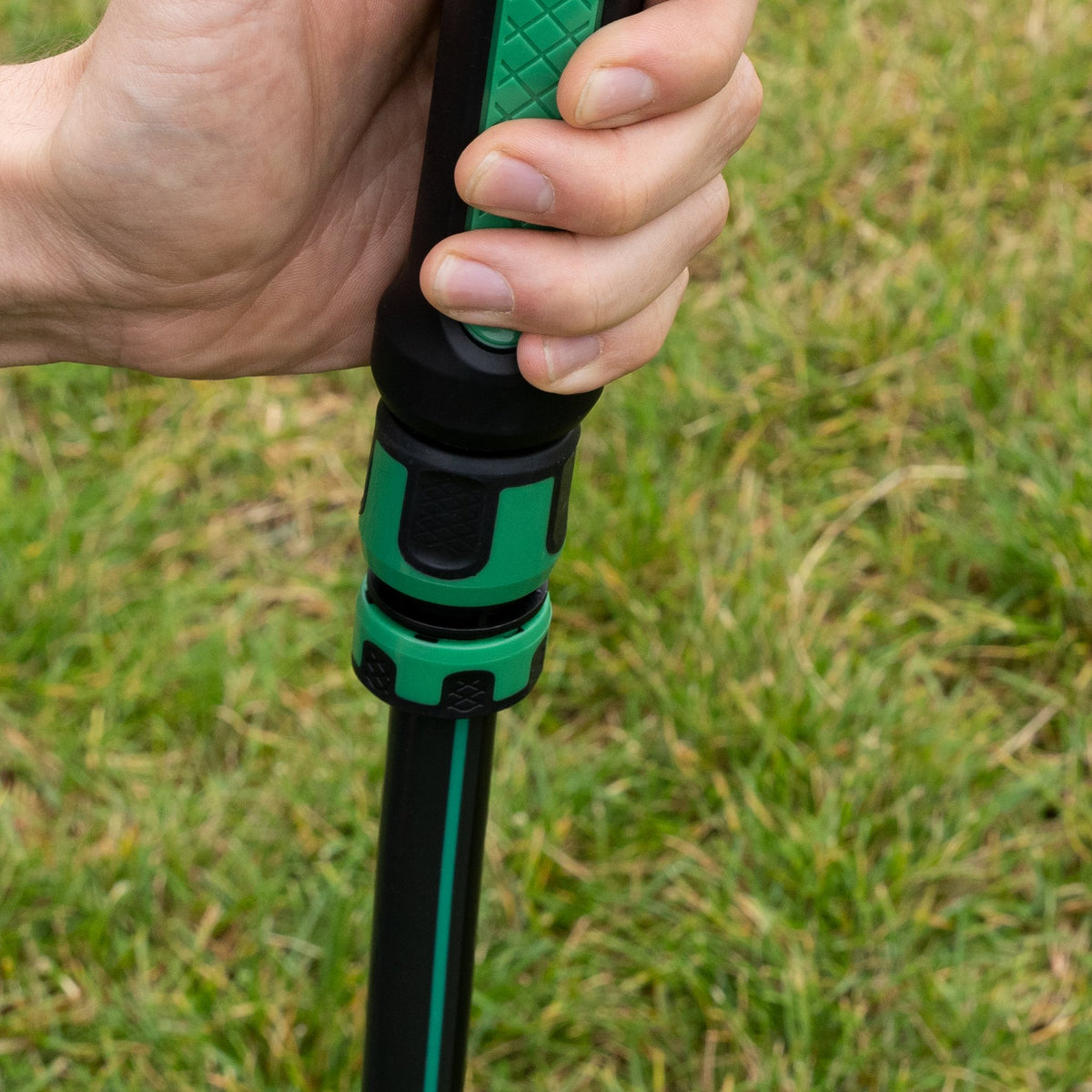 Steckverbinder am Gartenschlauch, aufgesteckt auf eine Gartenpistole in der Hand, Rasen im Hintergrund