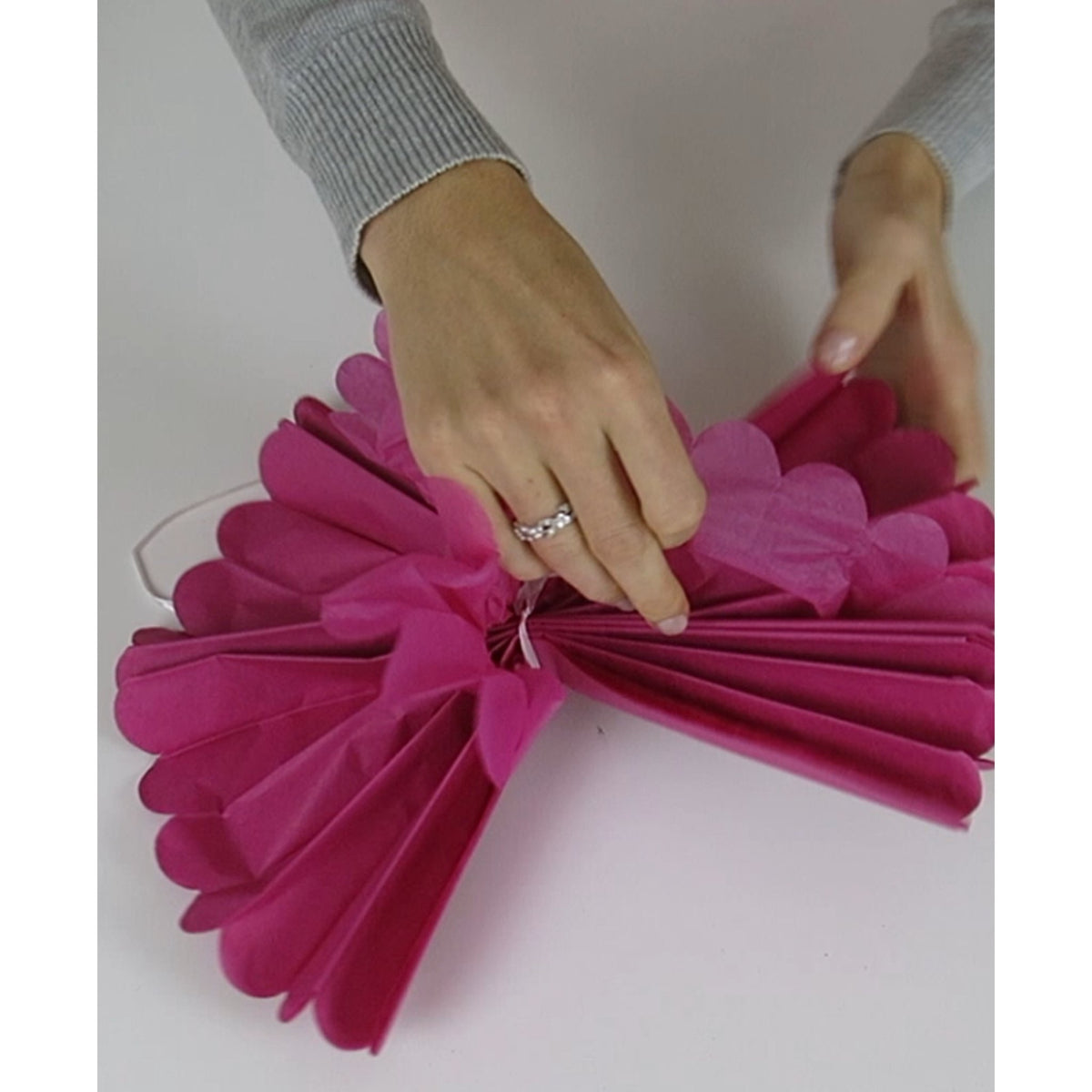 Hände falten einen pinken Seidenpapier-Pompon auf, die Pompons werden gefaltet geliefert