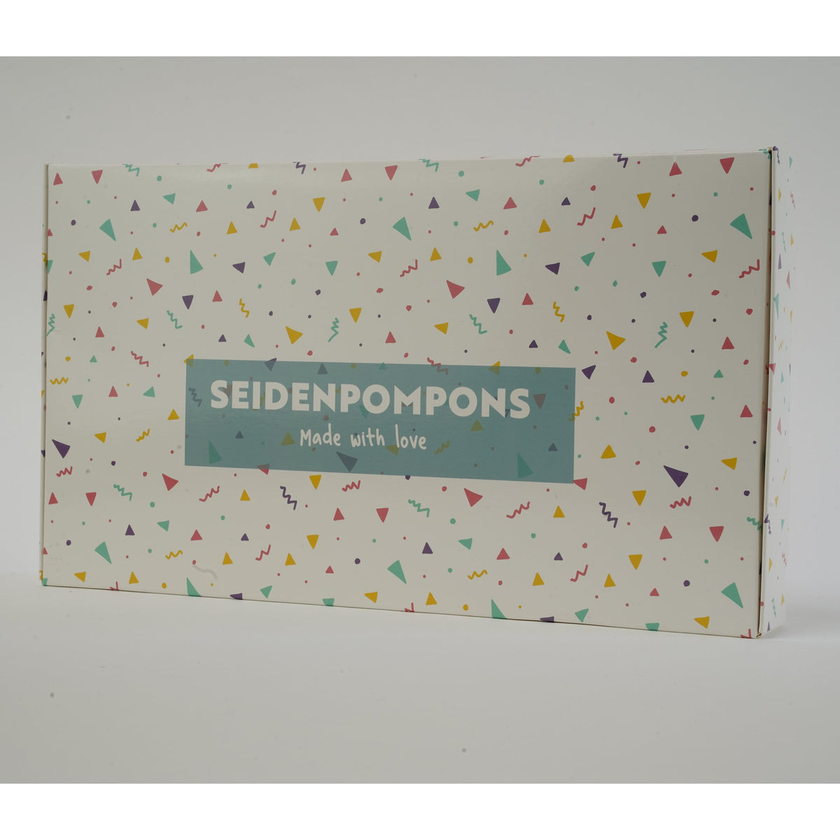 Geschenkbox mit Konfetti-Muster und Aufschrift Seidenpompons, in der die Pompons geliefert werden
